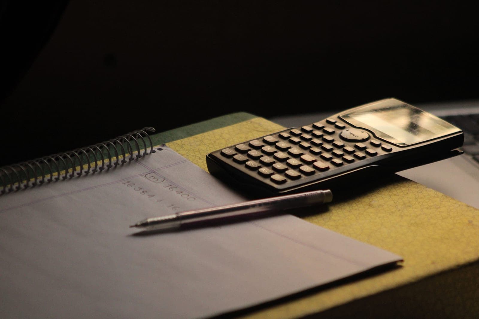 A notebook and pencil on a desk, part-way through a set of written calculations