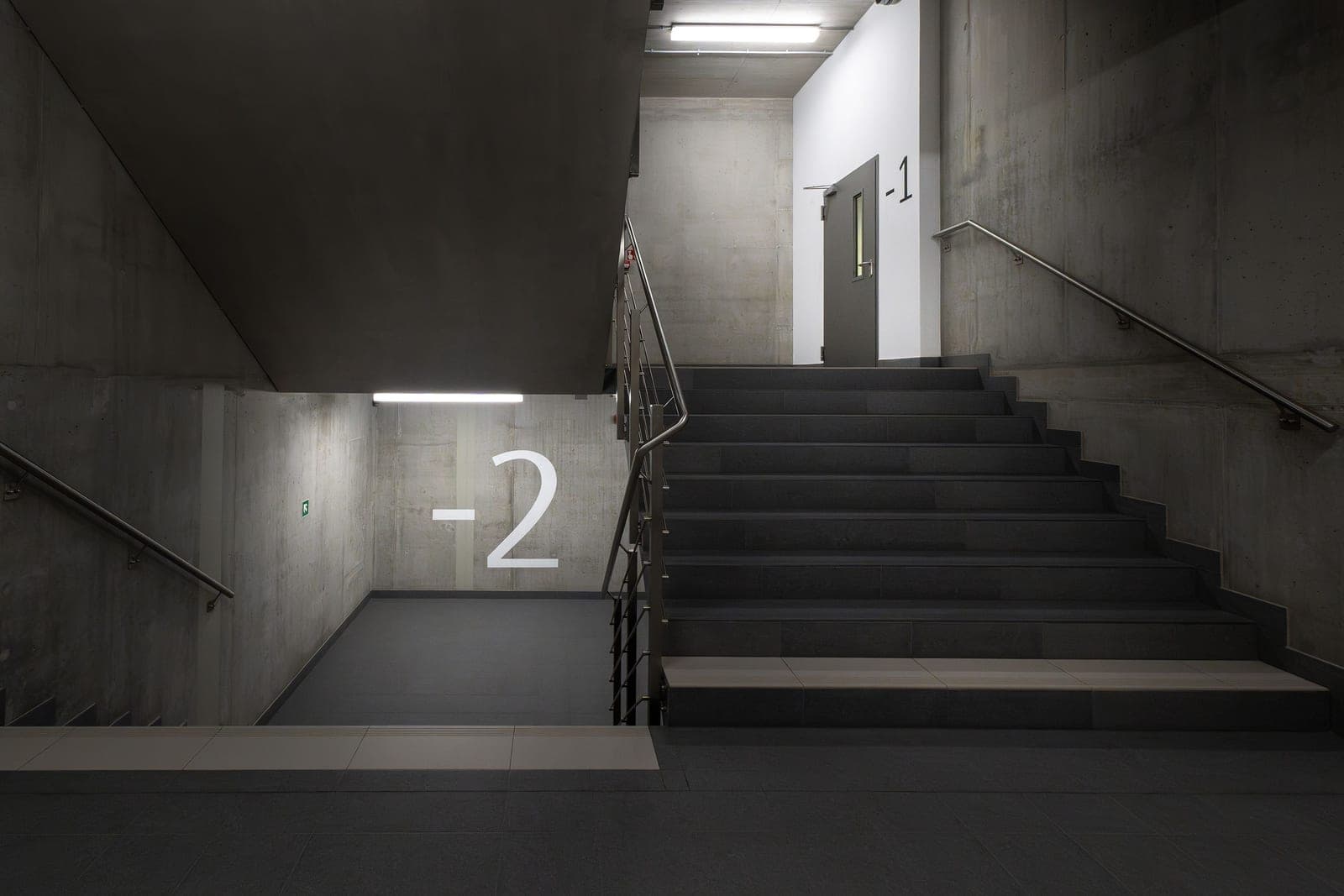 Concrete basement steps descending into dim light beside a painted foundation wall